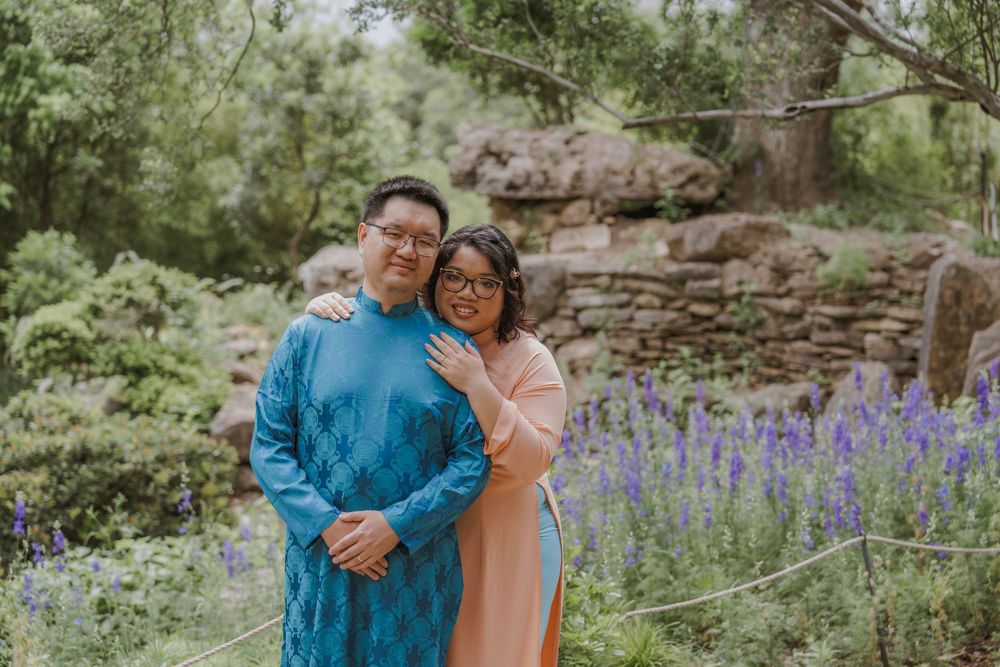 Couple posing near purple wildflowers in a lush garden setting.