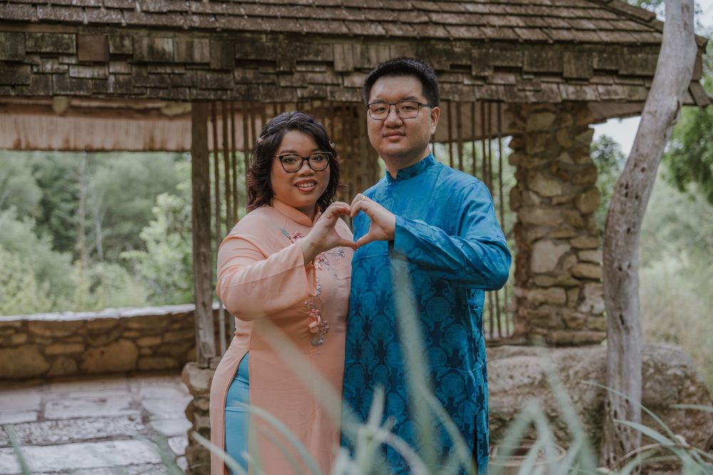 Two people make heart shapes with their hands against a garden backdrop.