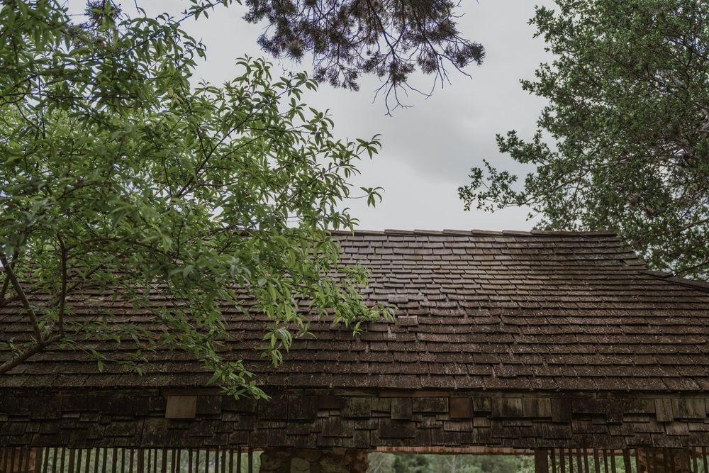 Stone garden structure with wooden beams viewed from below against cloudy sky.
