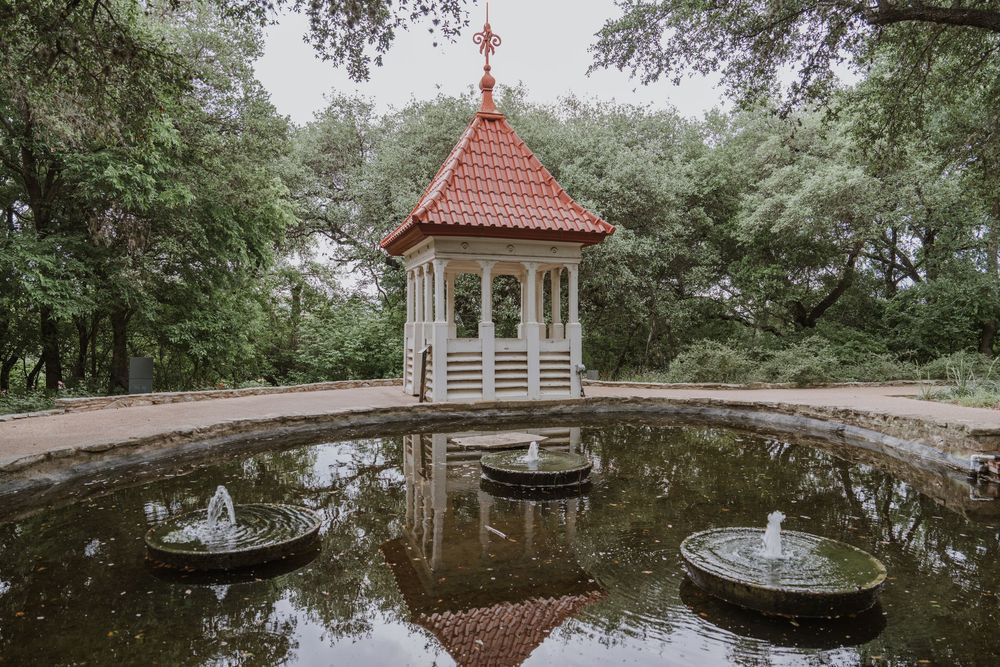 Serene garden landscape with red-roofed gazebos and reflective ponds surrounded by lush trees.