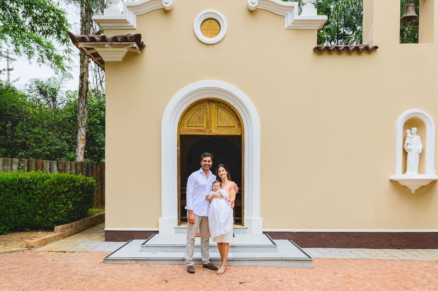 Couple in white outfits embracing in front of Mediterranean-style church entrance with arched doorway.