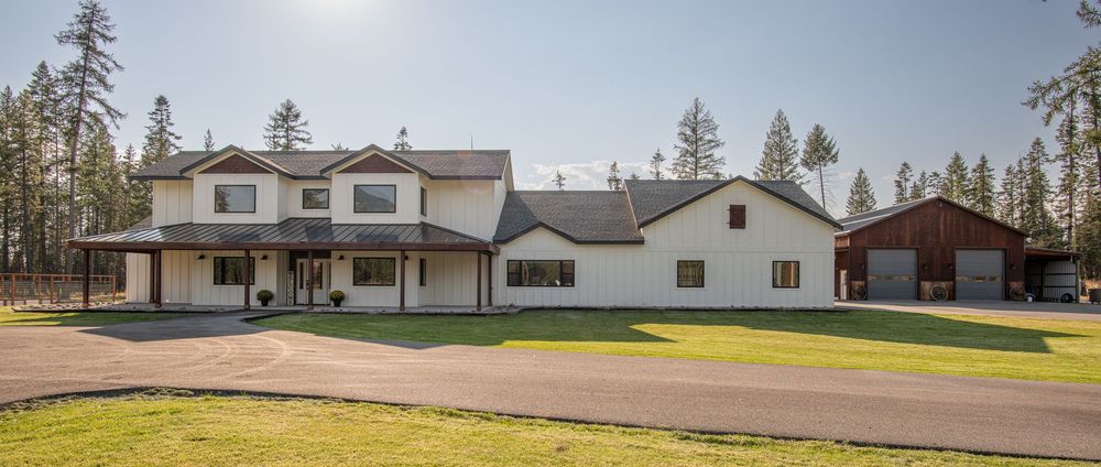 Modern residential homes with white exterior and attached garages sit along a rural property lined with tall pine trees.
