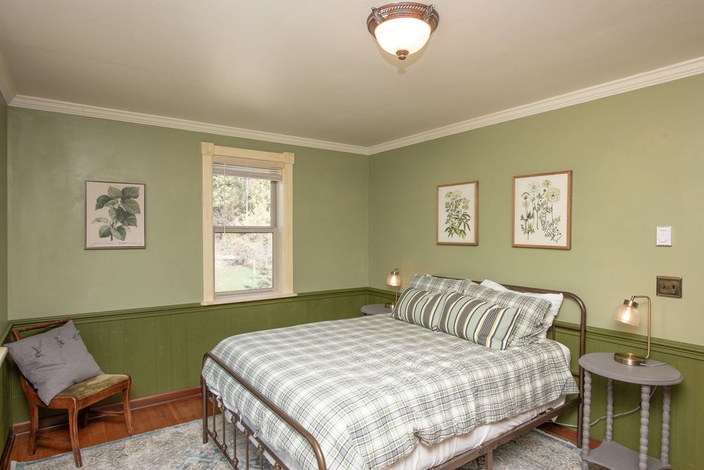 A cozy bedroom with sage green walls, plaid bedding, and framed artwork features warm lighting and traditional decor.