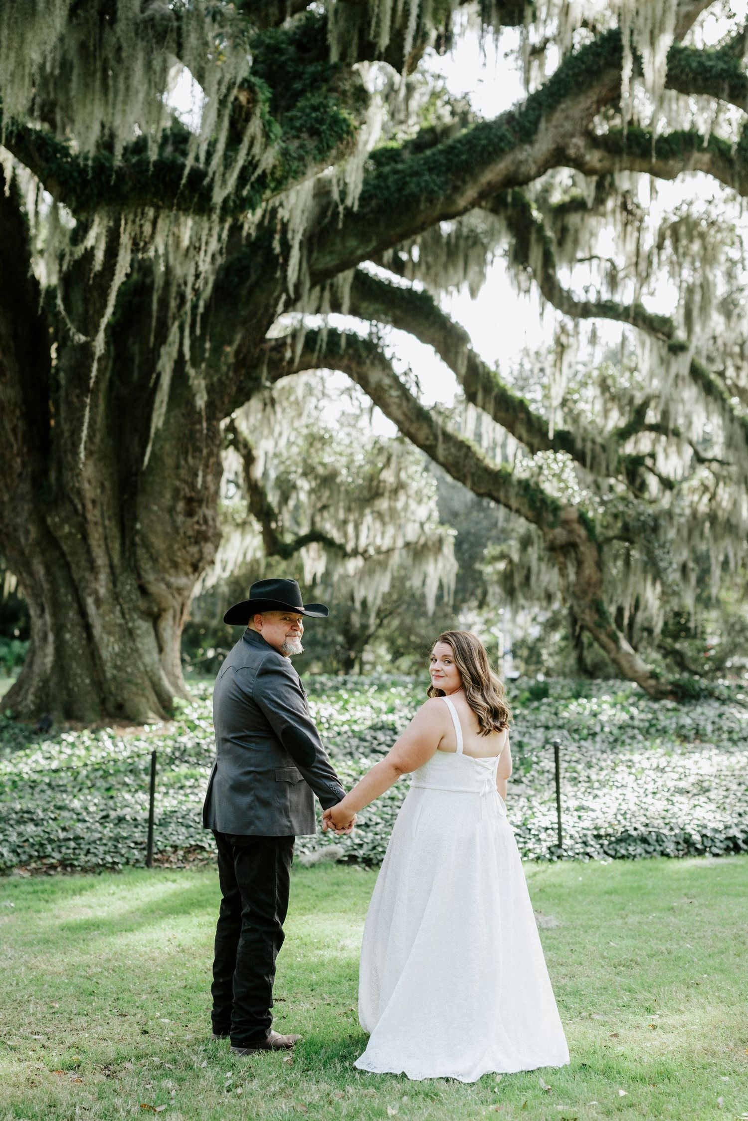 A romantic first look moment under Spanish moss draped trees in a garden setting.