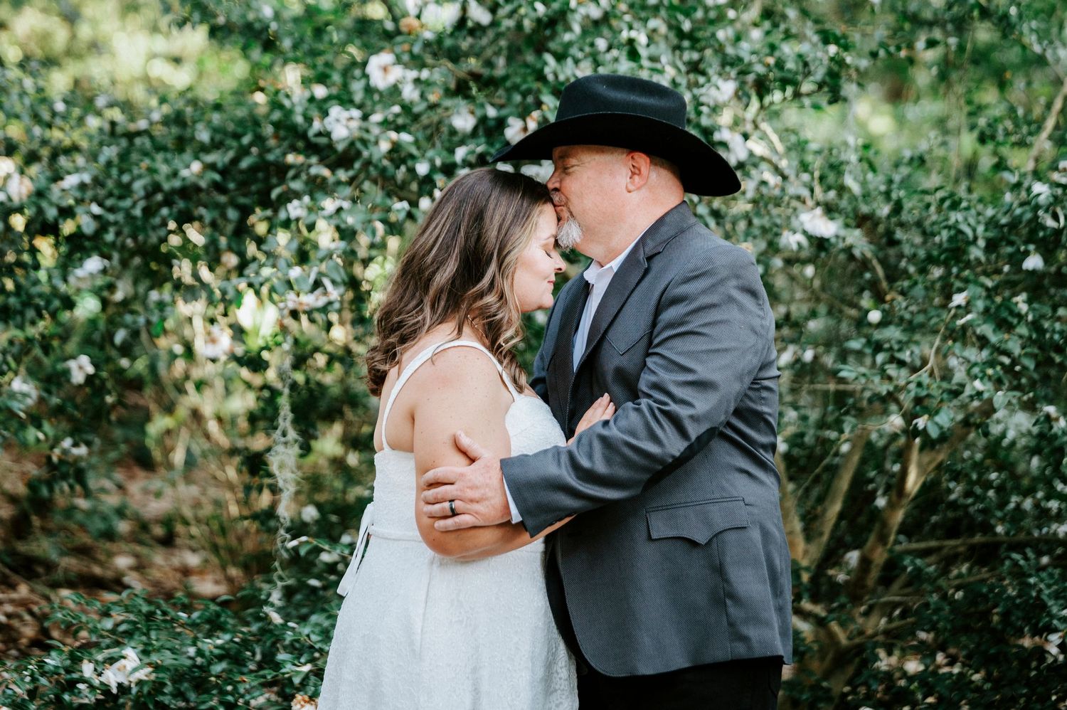 A romantic wedding couple embraces in front of lush green foliage during an outdoor photo session.