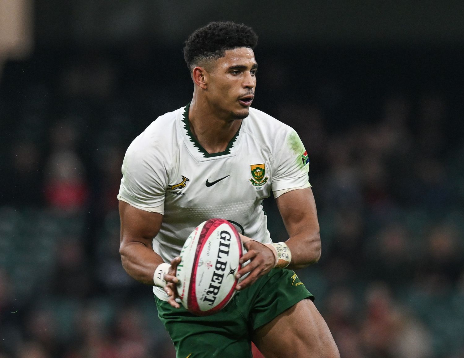 Rugby player in white uniform carries ball during match on green field at stadium.