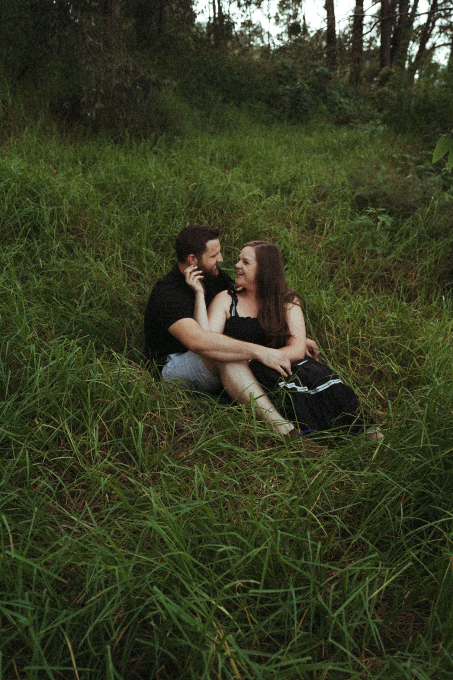 Couple lying together in tall grass during an outdoor photoshoot.