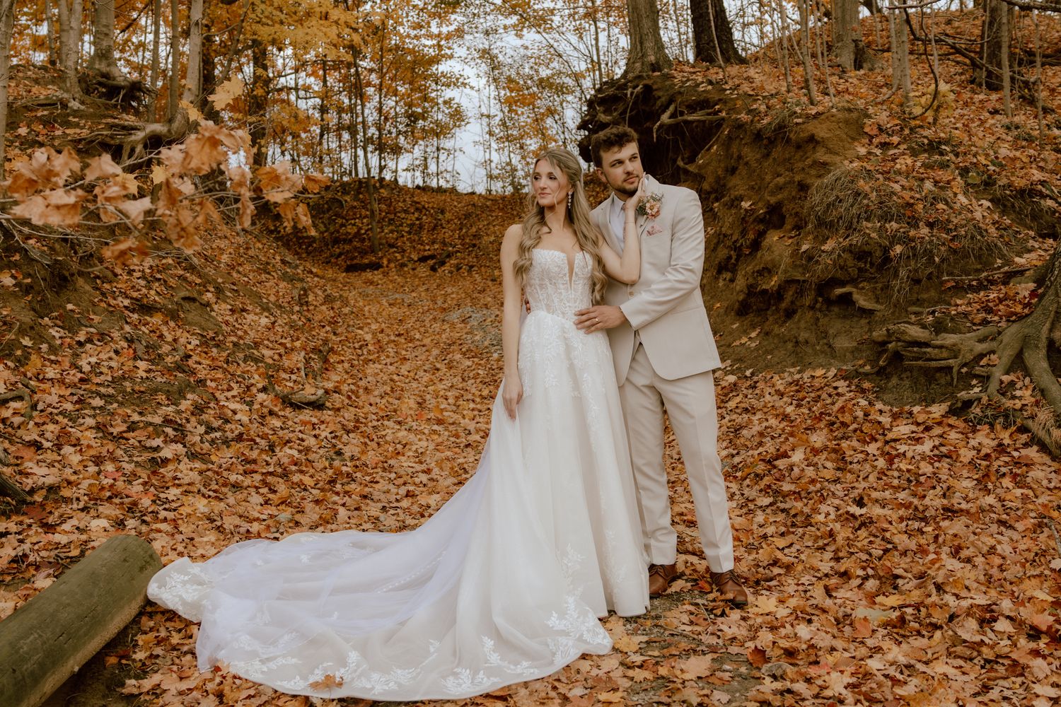 Bride and groom embracing in a forest path covered in vibrant orange autumn leaves.
