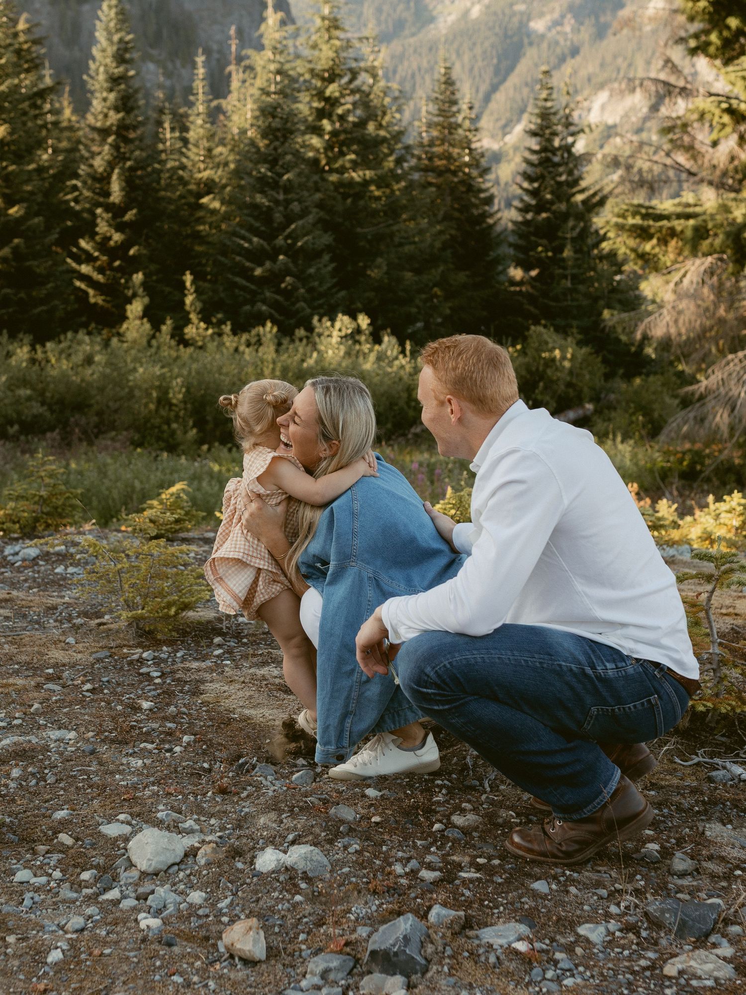 Couple sitting close together on rocky mountain terrain during golden hour in a forest setting.