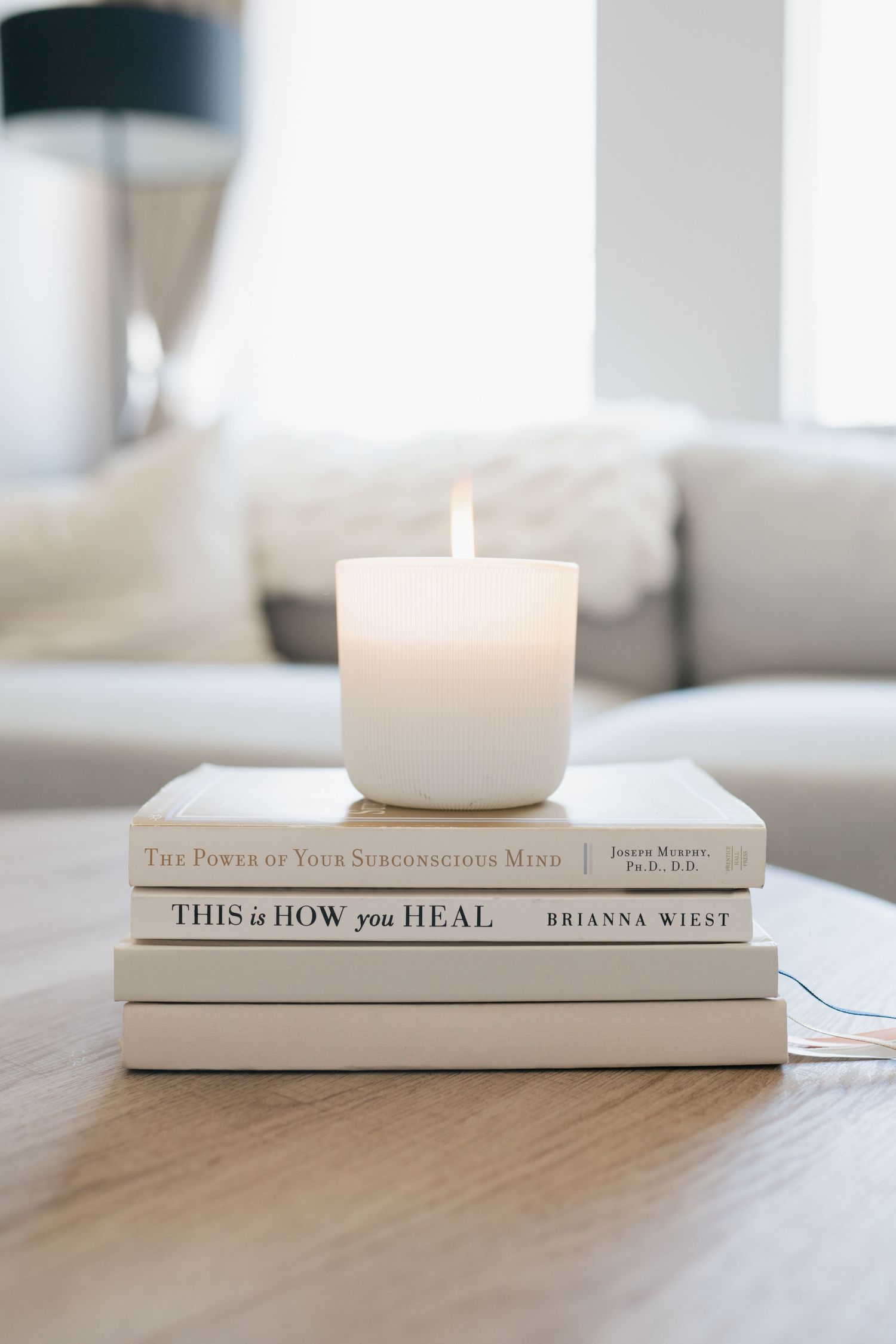 White minimalist books and candle arranged on table creating a serene aesthetic display in neutral tones.