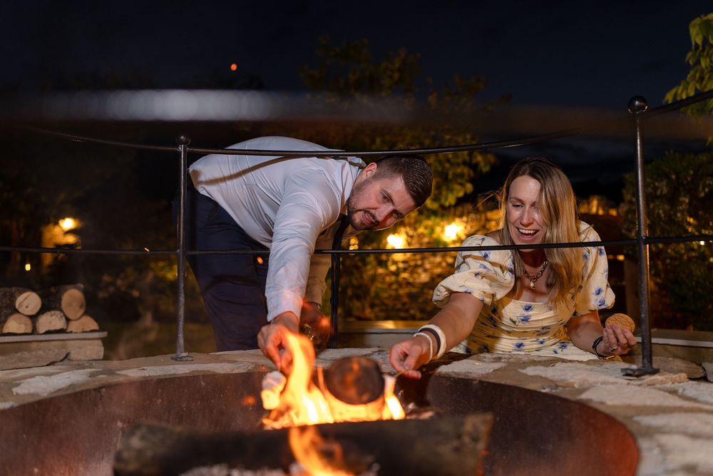 Outdoor evening gathering with fire pit and people socializing around tables.