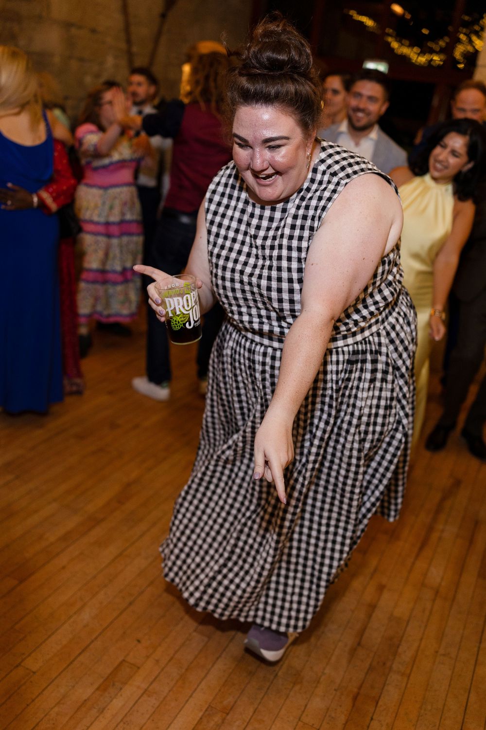 Person in a black and white checkered dress dances energetically on a wooden dance floor at a party.