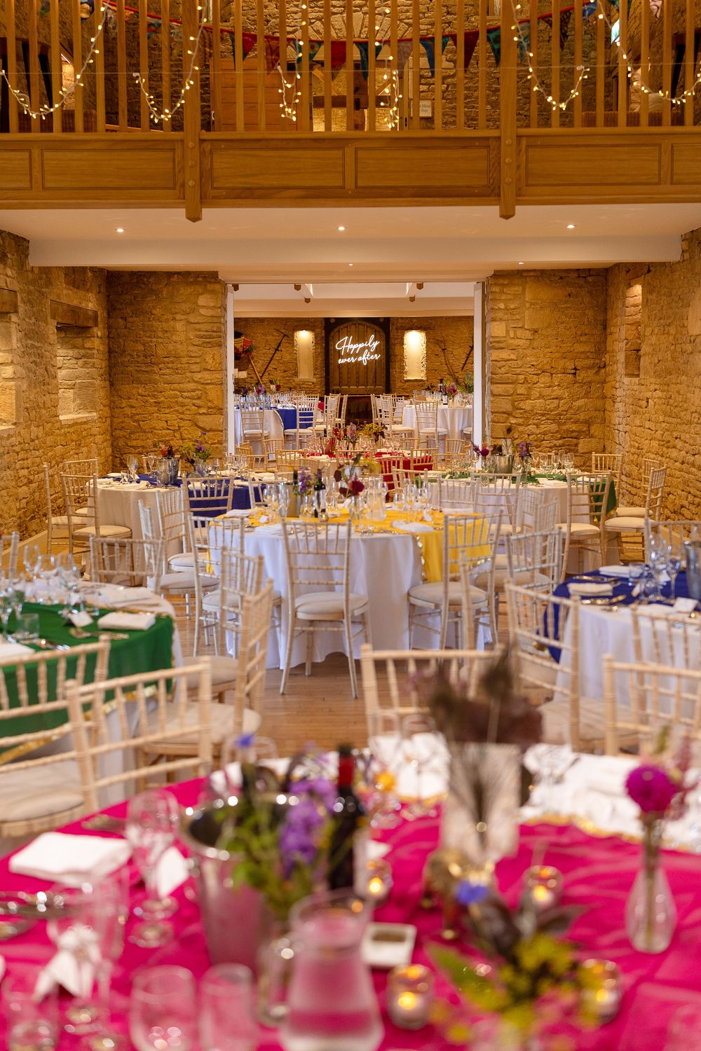 Elegant wedding reception venue with stone walls, white chiavari chairs, and vibrant pink floral centerpieces on dining tables.