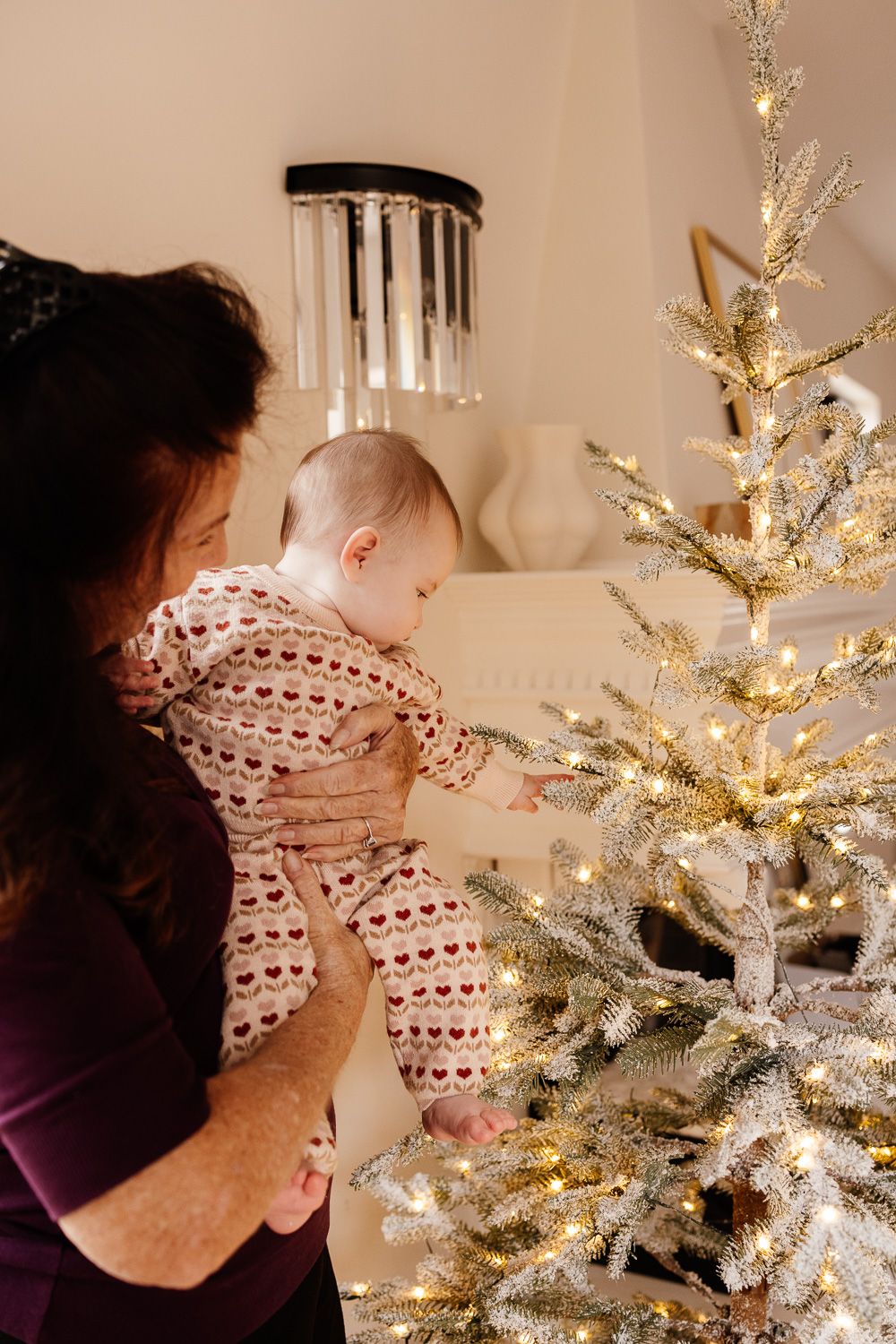 Baby reaches for the Christmas tree while being held by a woman