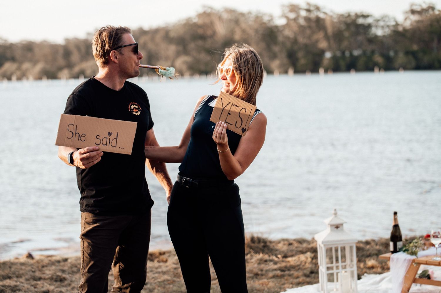 Couple in black outfits walking together near a lake during sunset creating a romantic silhouette.