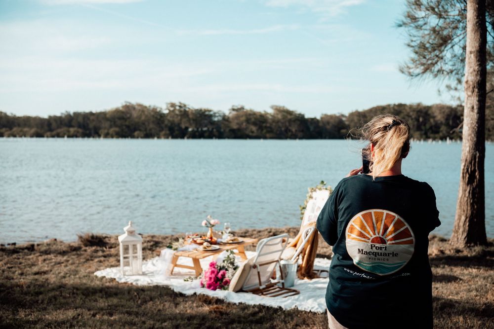 People enjoying a scenic lakeside view with trees and water stretching to the horizon on a calm day.