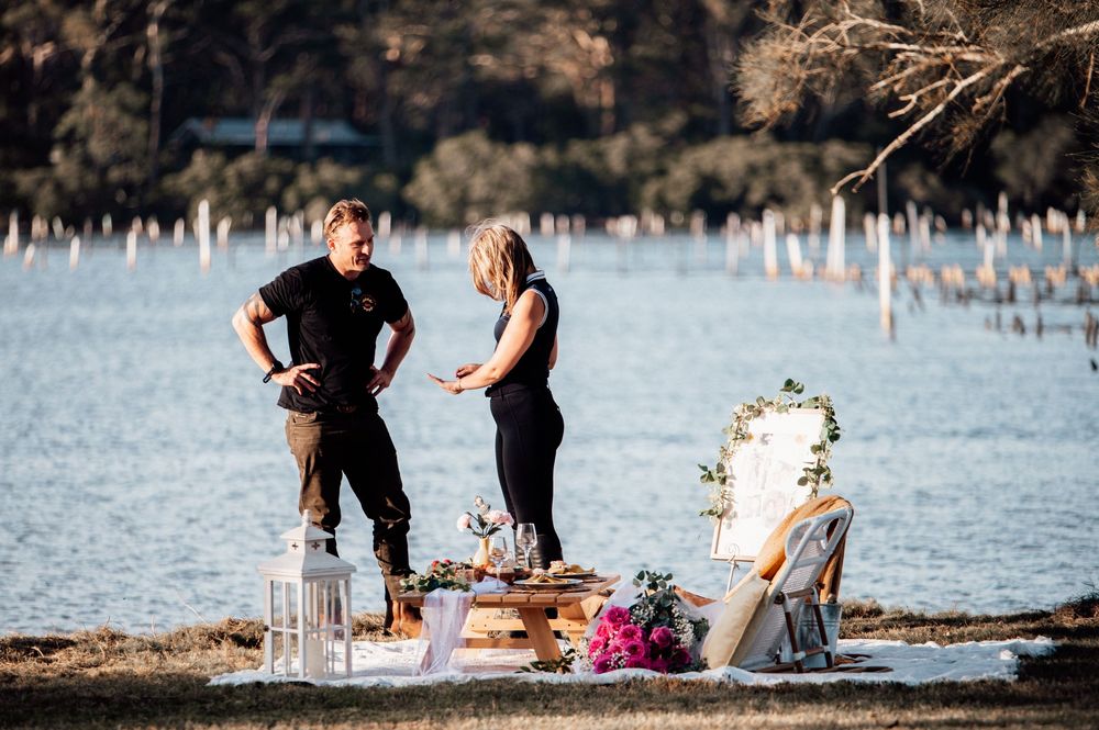 People enjoying a romantic lakeside picnic with wine glasses and snacks at sunset.