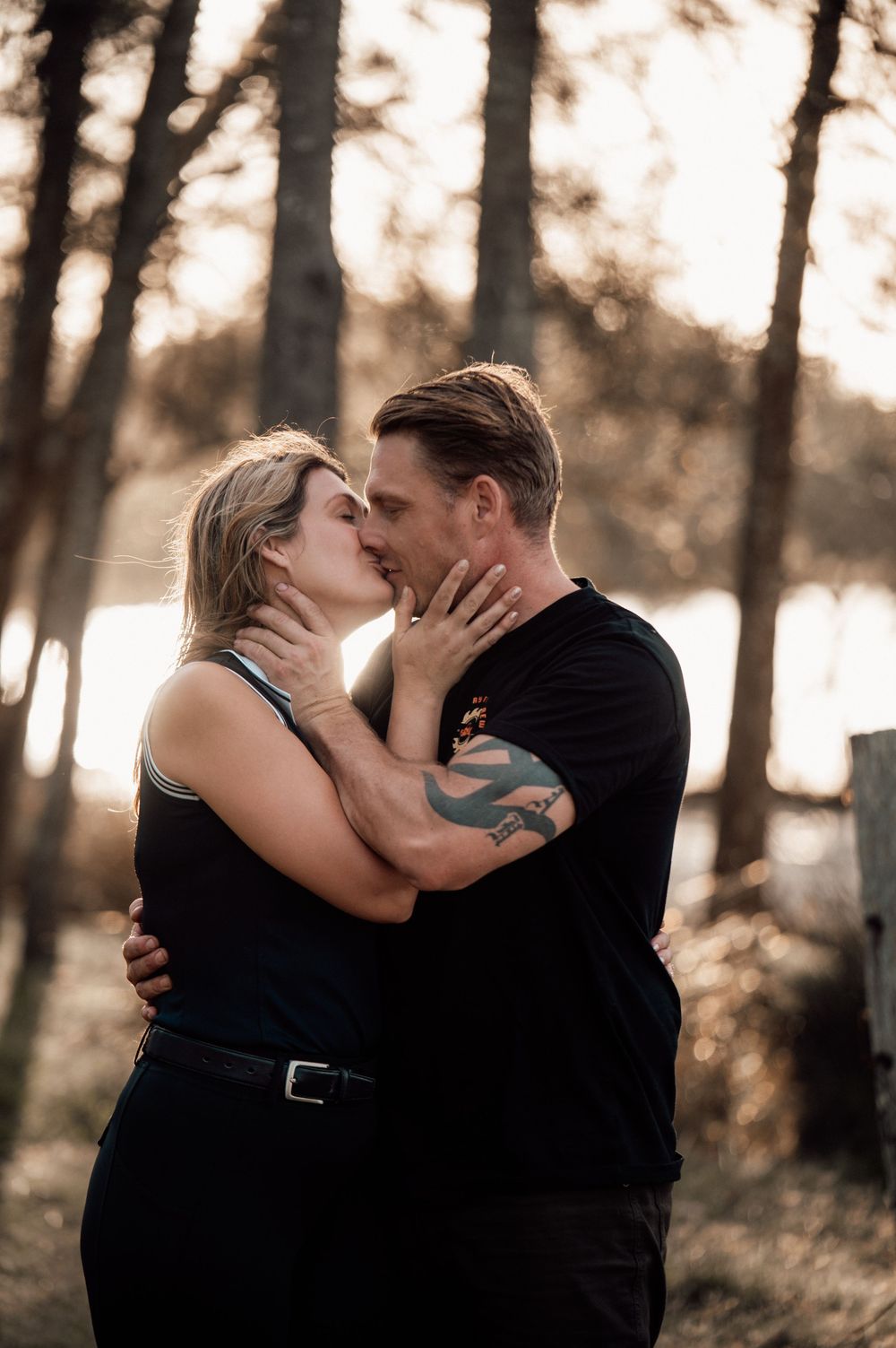 A romantic couple shares intimate kisses in a wooded setting during golden hour.