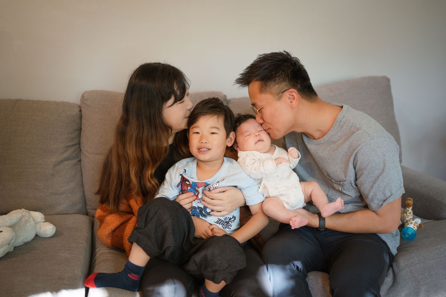 A family shares a tender moment on their sofa, cuddling close with their children.