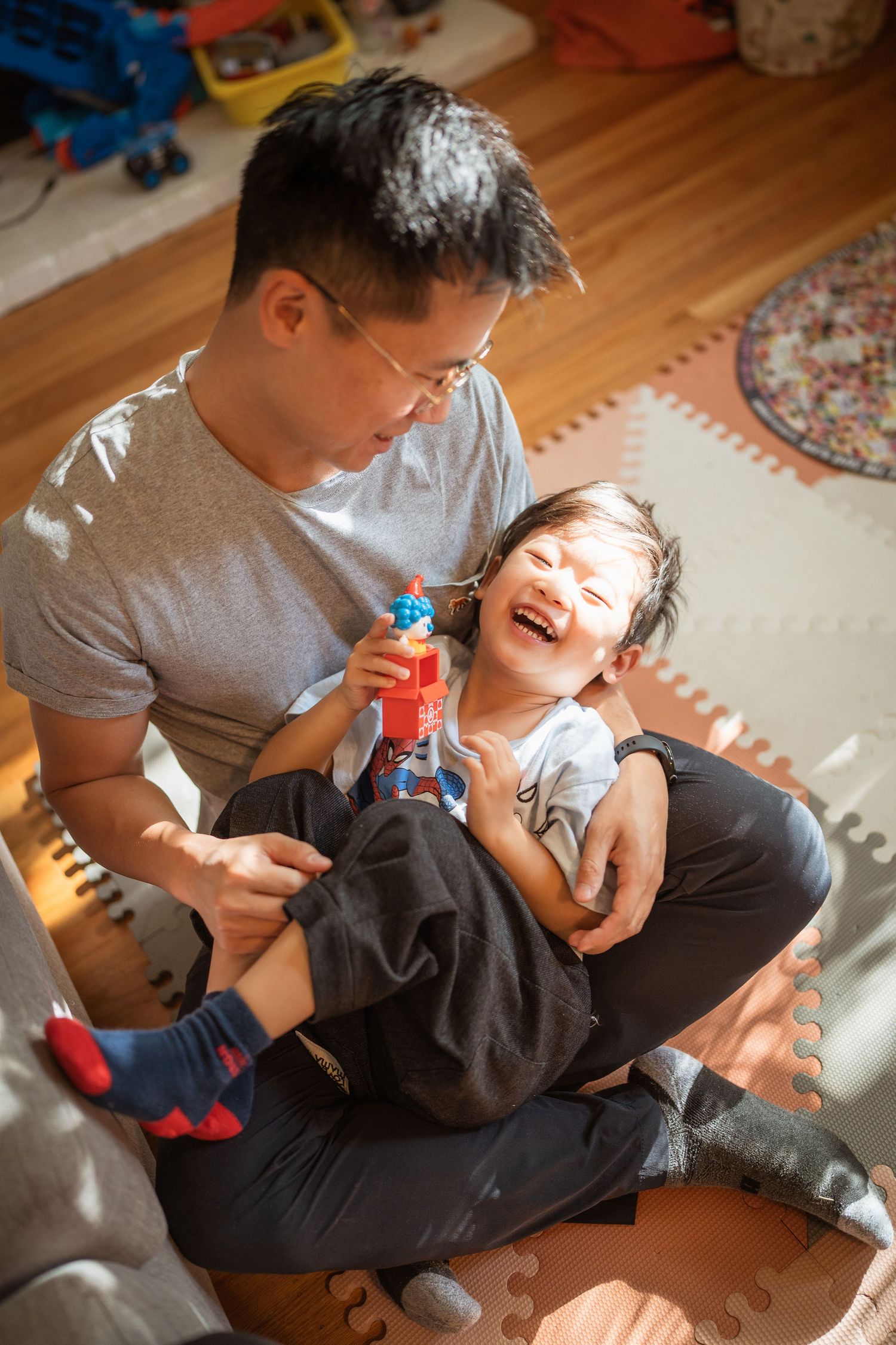 Parent and child share playful moment on wooden floor with toys.