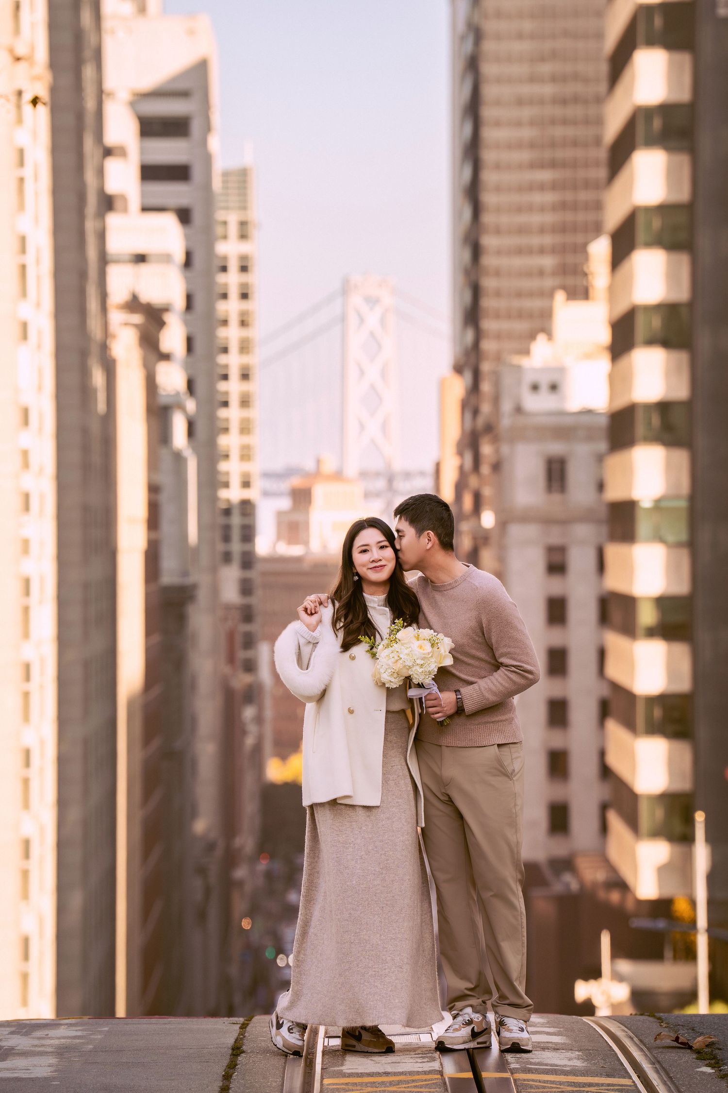 A couple shares a tender moment in front of tall urban buildings during golden hour.