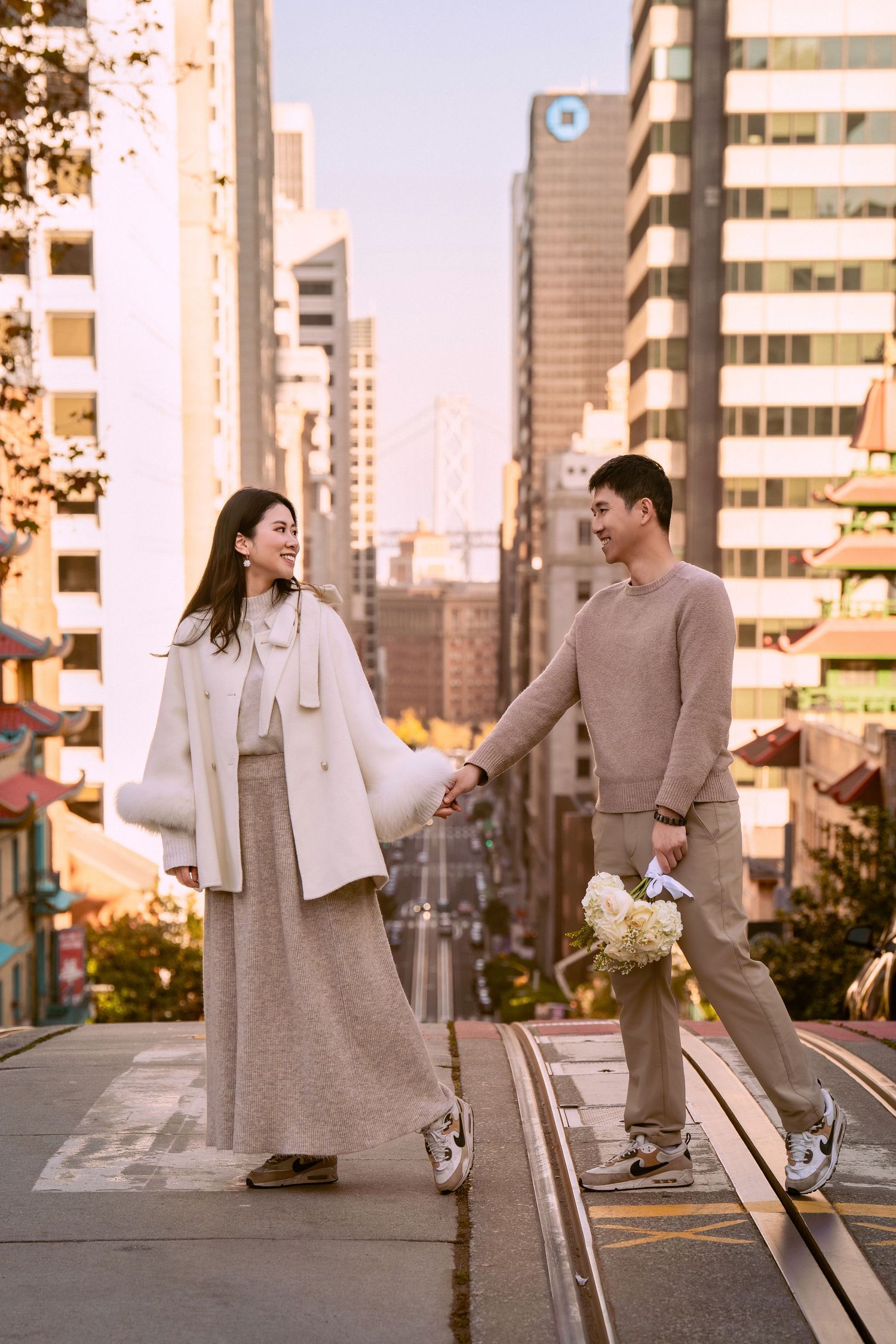 A couple shares a playful moment on a city rooftop at sunset, with urban buildings in the background.