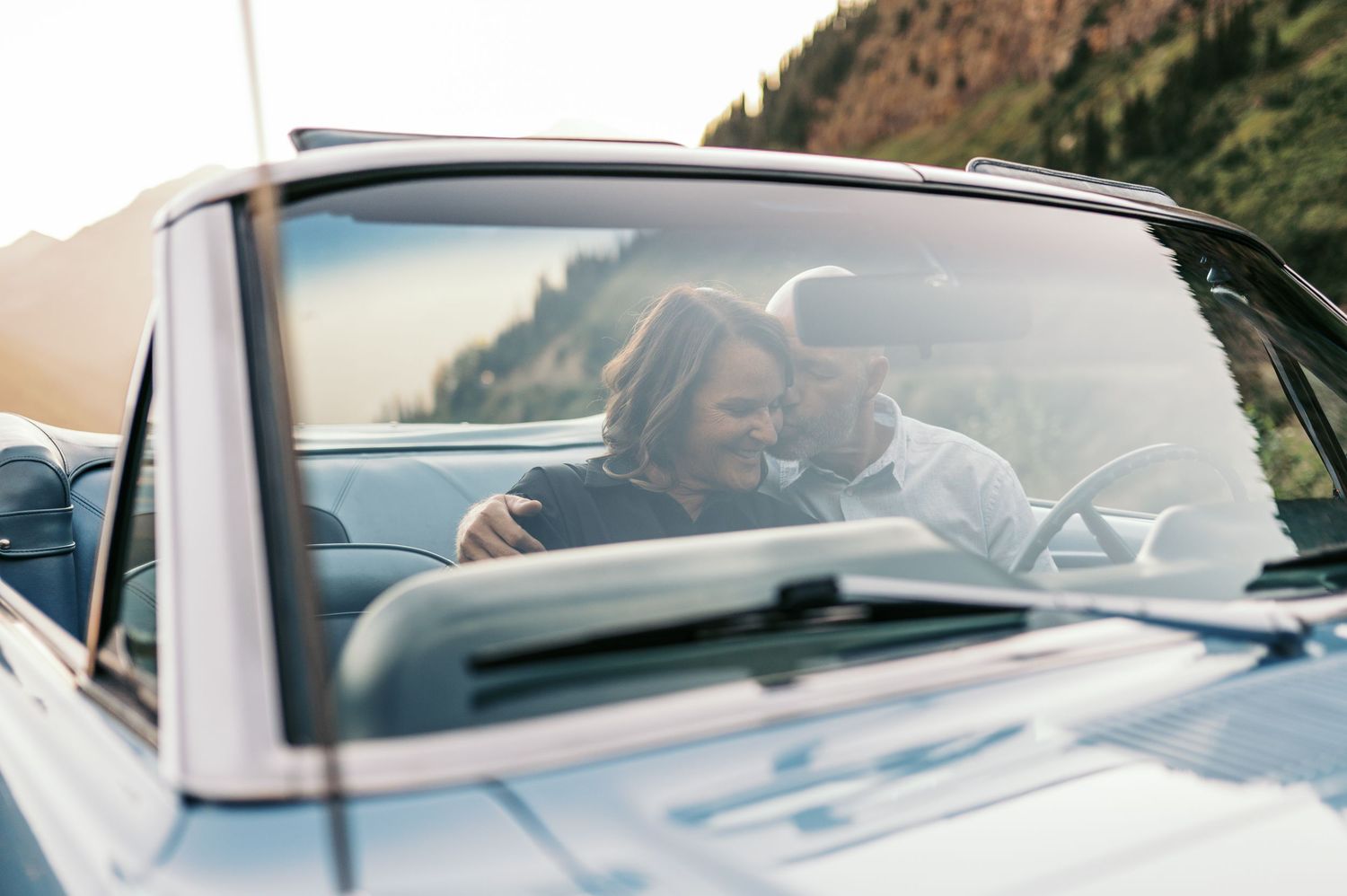 A car window is rolled down as someone drives along a scenic mountain road on a sunny day.