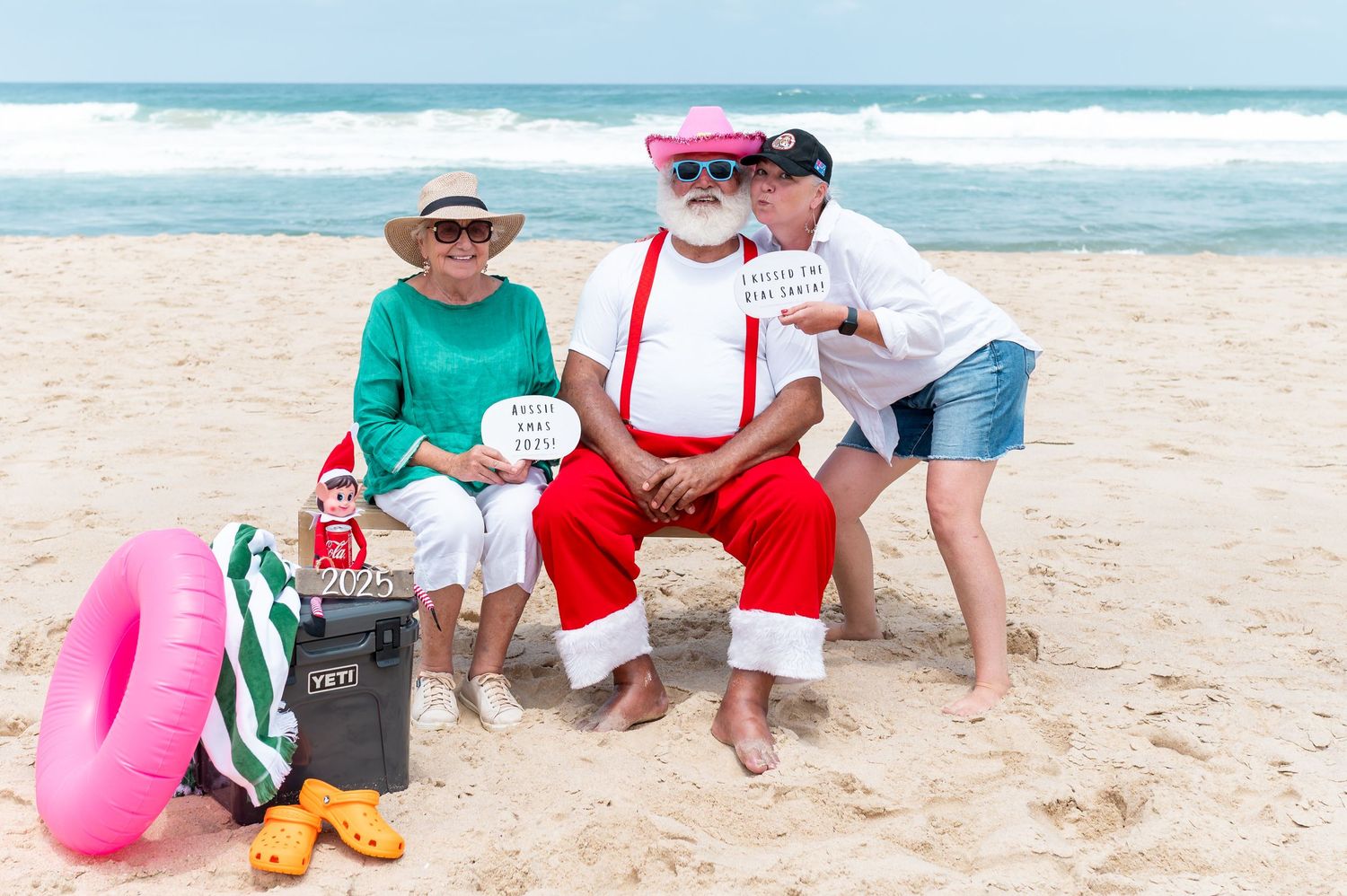 Festive holiday decorations adorn a beachside setting with red ribbons and ornaments against a sandy coastal backdrop.