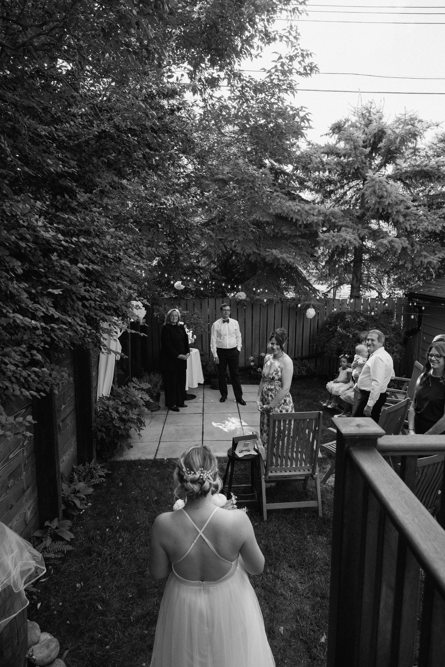 A sequence of black and white photos showing a backyard wedding ceremony with guests seated on benches and a wooden deck.