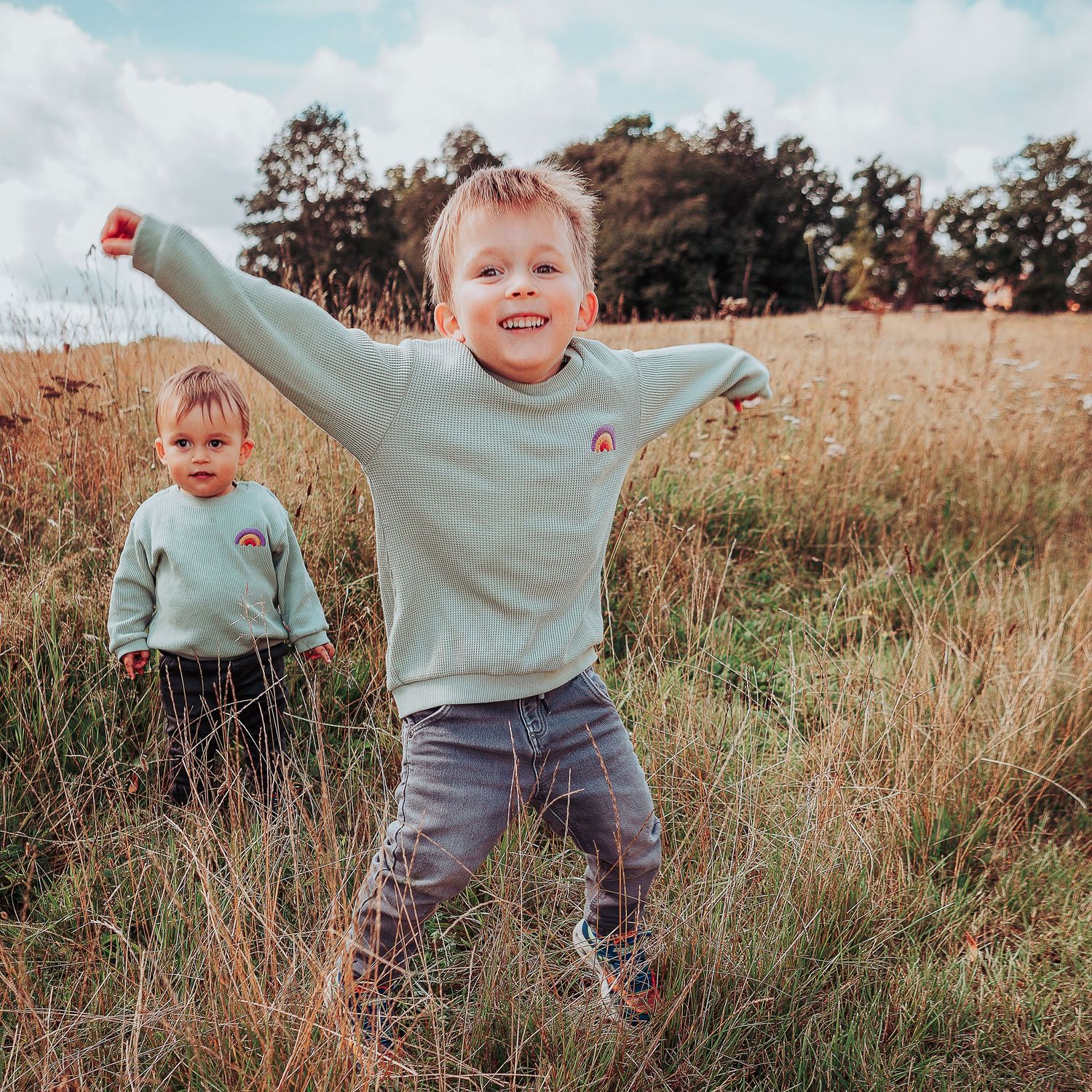Two boys jumping and playing in a meadow with matching jumpers.