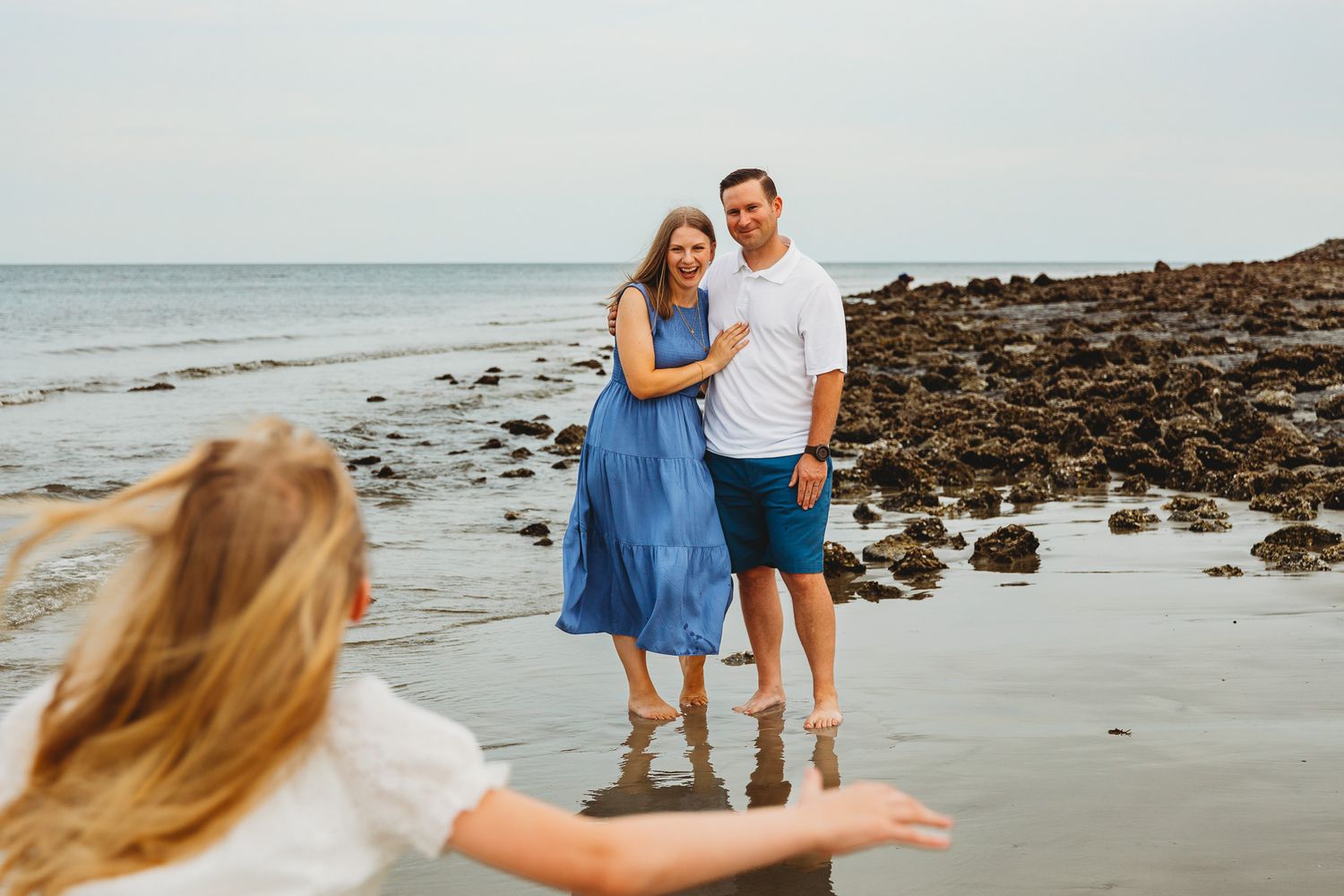 Couple walking and playing together on a rocky beach at sunset.