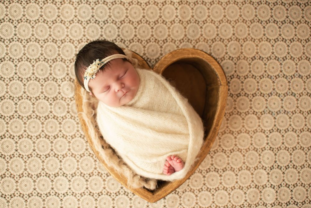 Newborn baby sleeping in wooden bowl against patterned backdrop.