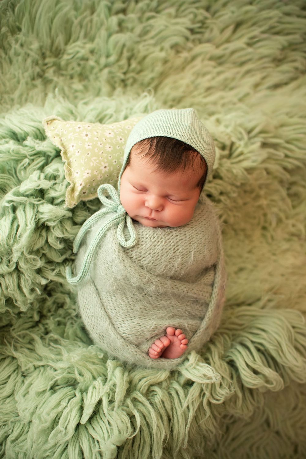 Newborn baby wrapped in soft mint green knit on fluffy green backdrop.