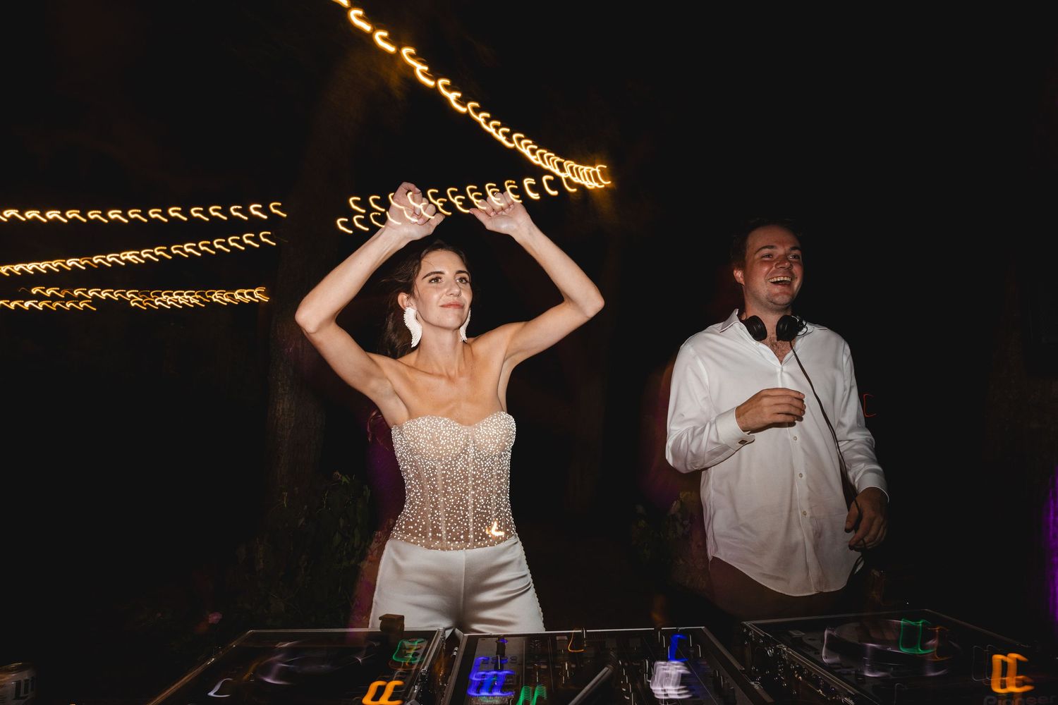 People dancing and celebrating at a nighttime party with string lights overhead creating a festive atmosphere.