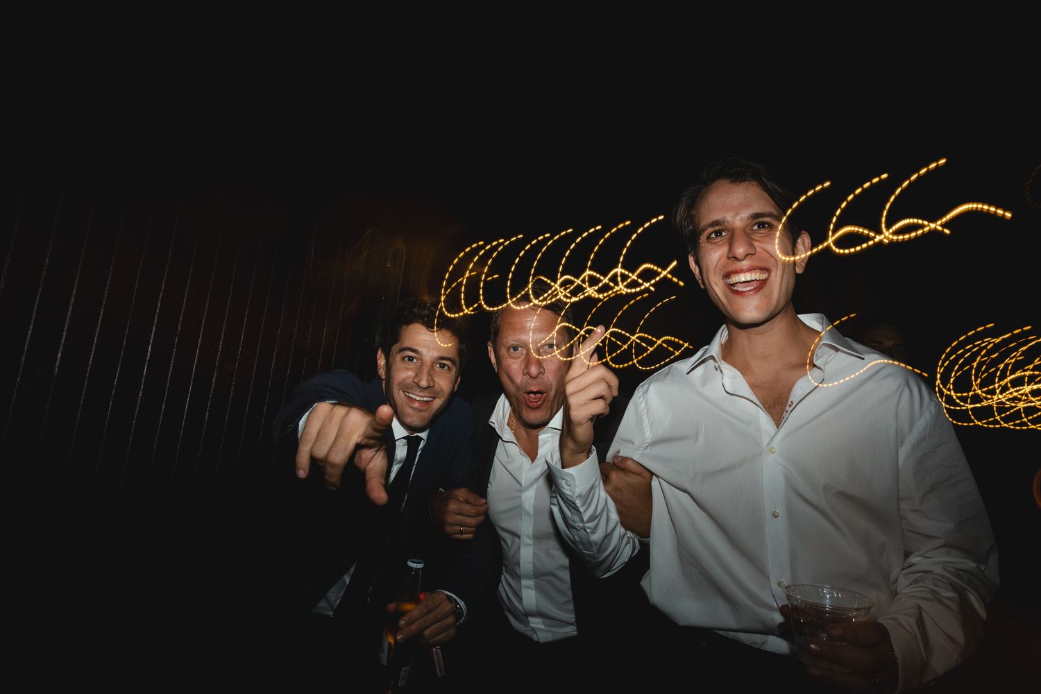 People dancing at a nighttime party with blurred light trails creating a festive atmosphere.
