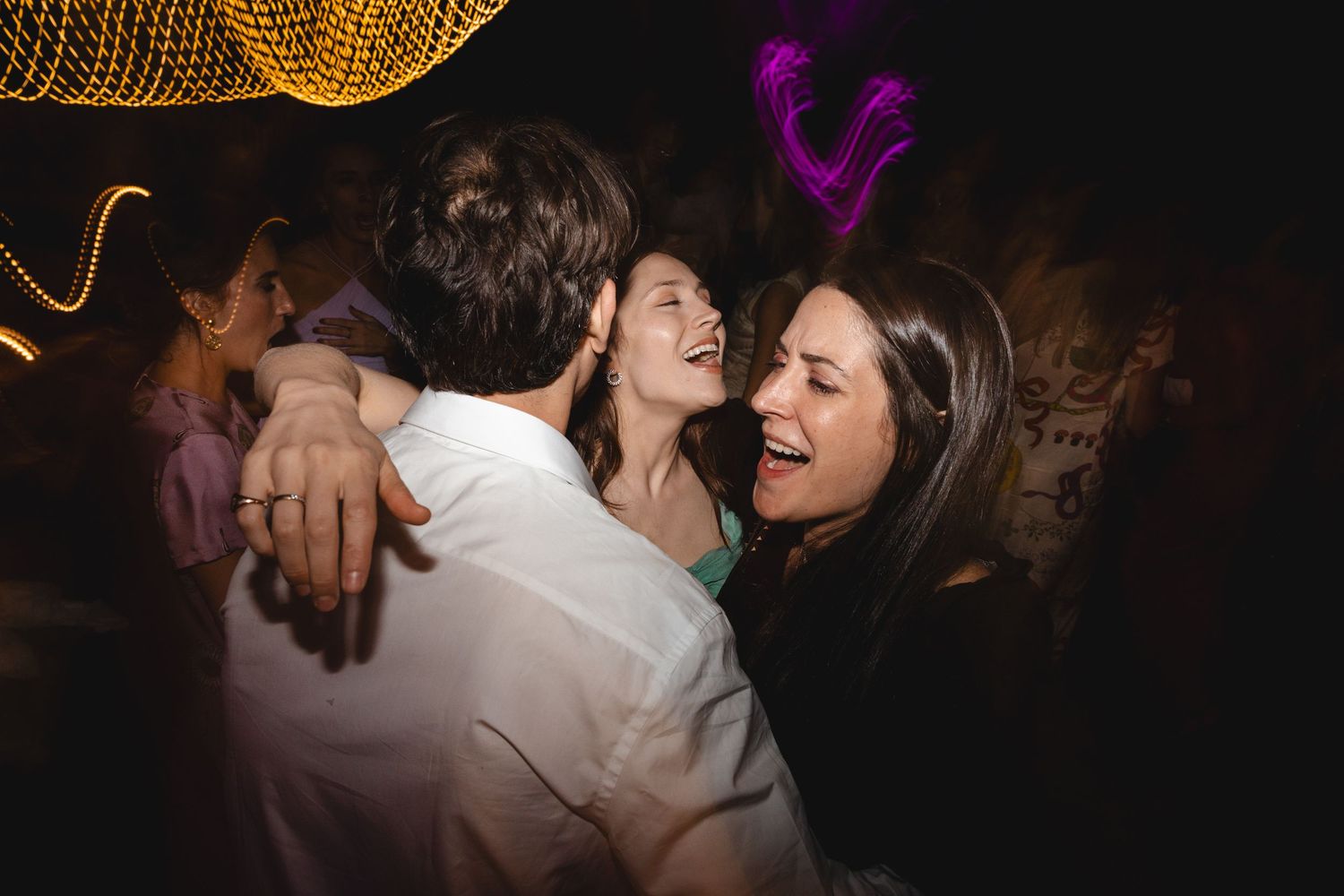 Couples dancing together at a dimly lit party with a disco ball overhead.