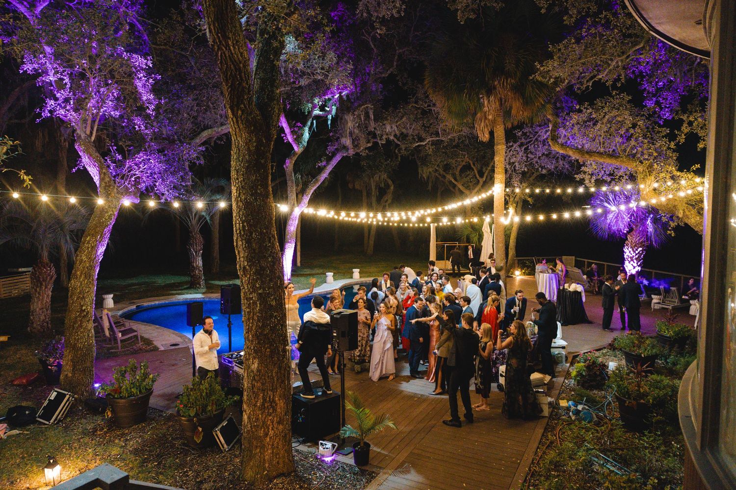 Outdoor wedding reception at night with purple uplighting on trees and string lights creating a magical atmosphere.