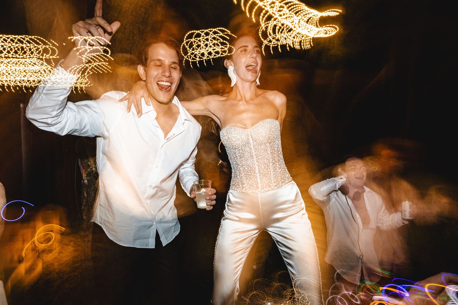 Wedding party guests dancing and celebrating on a dimly lit dance floor with warm lighting and festive atmosphere.