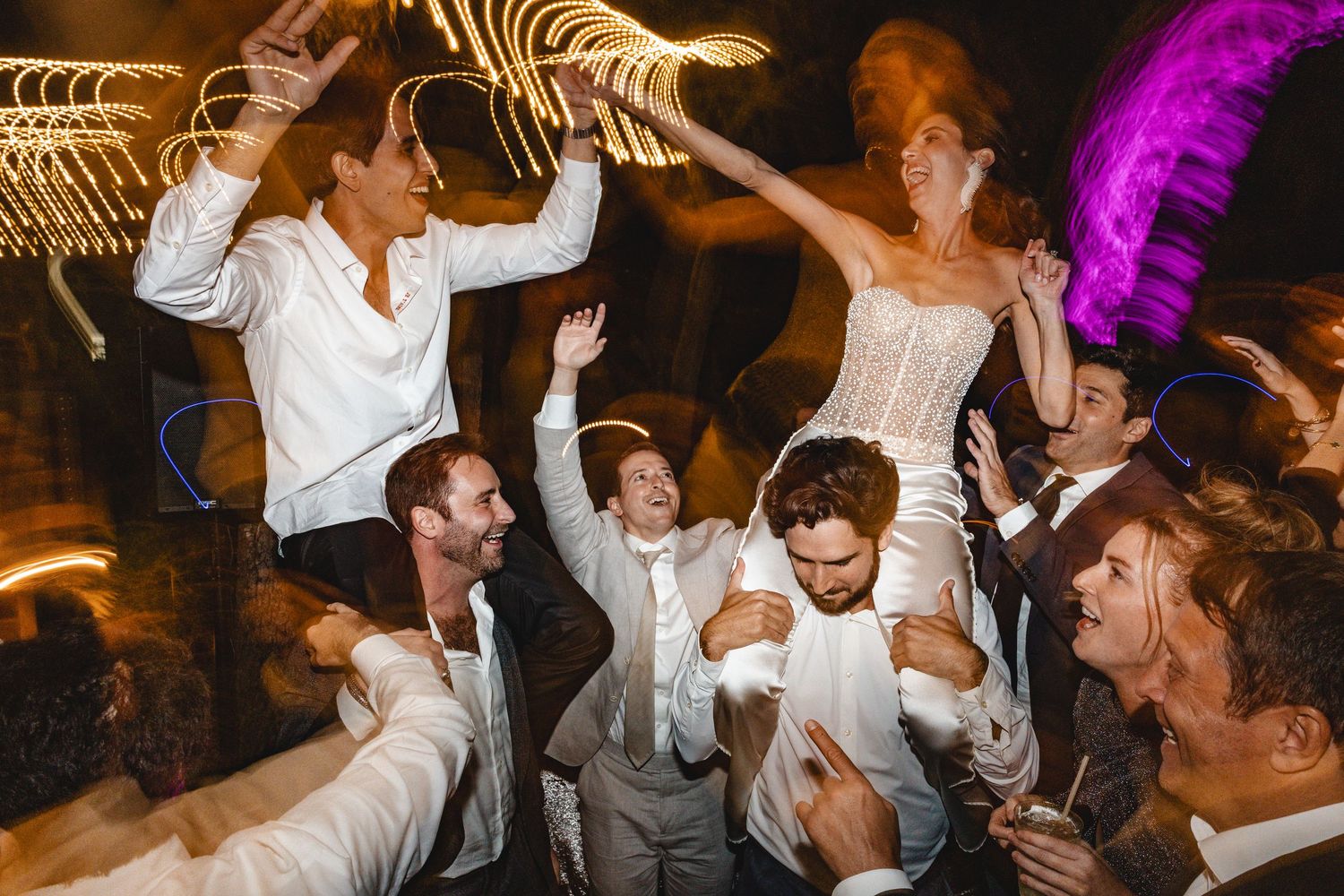 Wedding party dancing and celebrating at a reception with dramatic lighting and energetic movements.