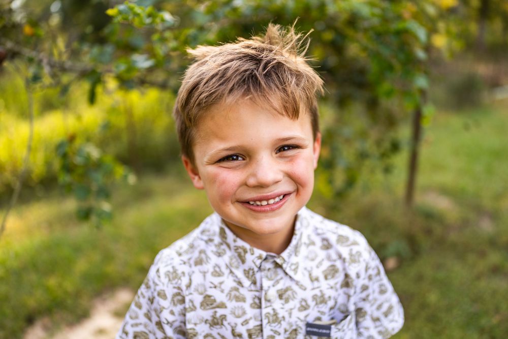 A child smiling and posing outdoors against a green natural background.