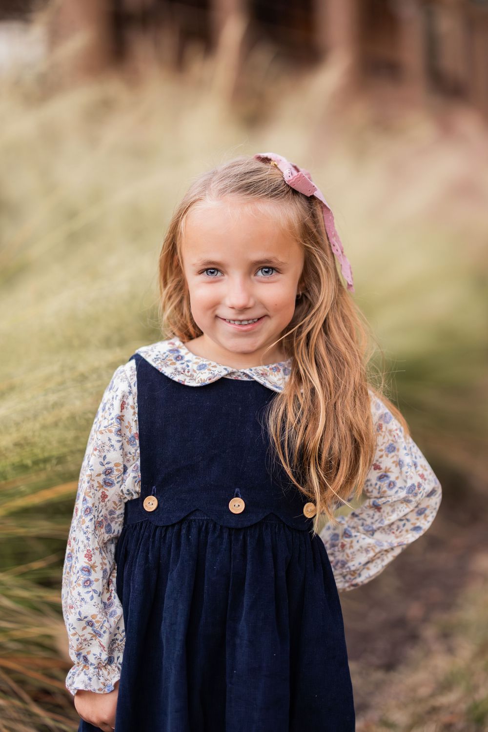 A young person in a navy pinafore dress with floral sleeves poses outdoors.