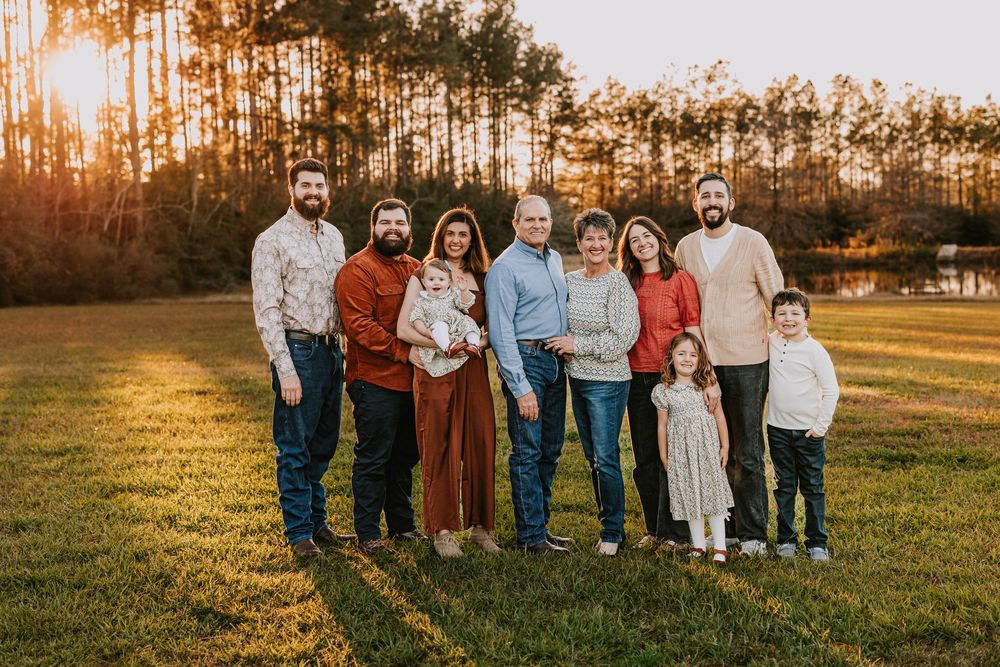 Extended family group poses together at sunset with pine trees in the background.