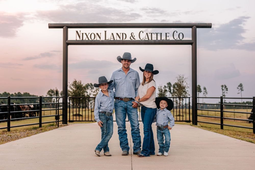 A family stands beneath a ranch entrance sign reading Nixon Land & Cattle Co at sunset.