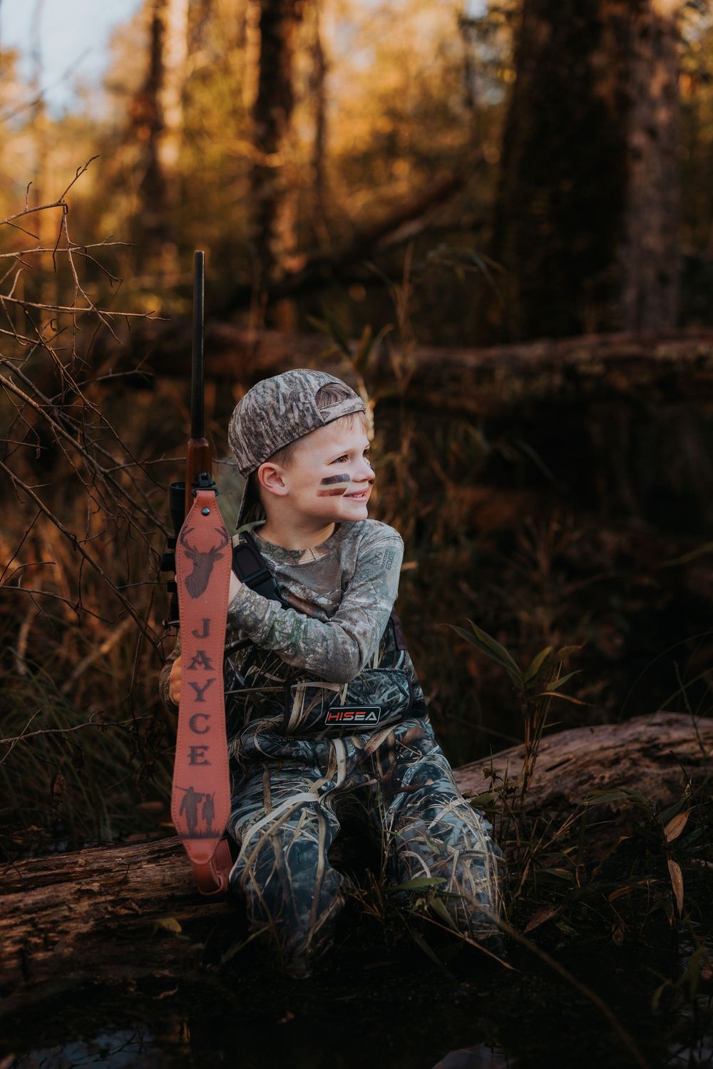 A hunter in camo gear positions themselves behind trees during golden hour.