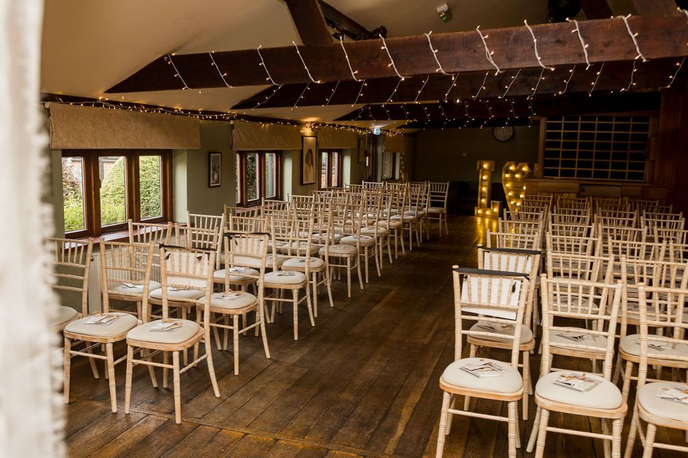 Empty wedding ceremony venue with white chairs and string lights overhead.