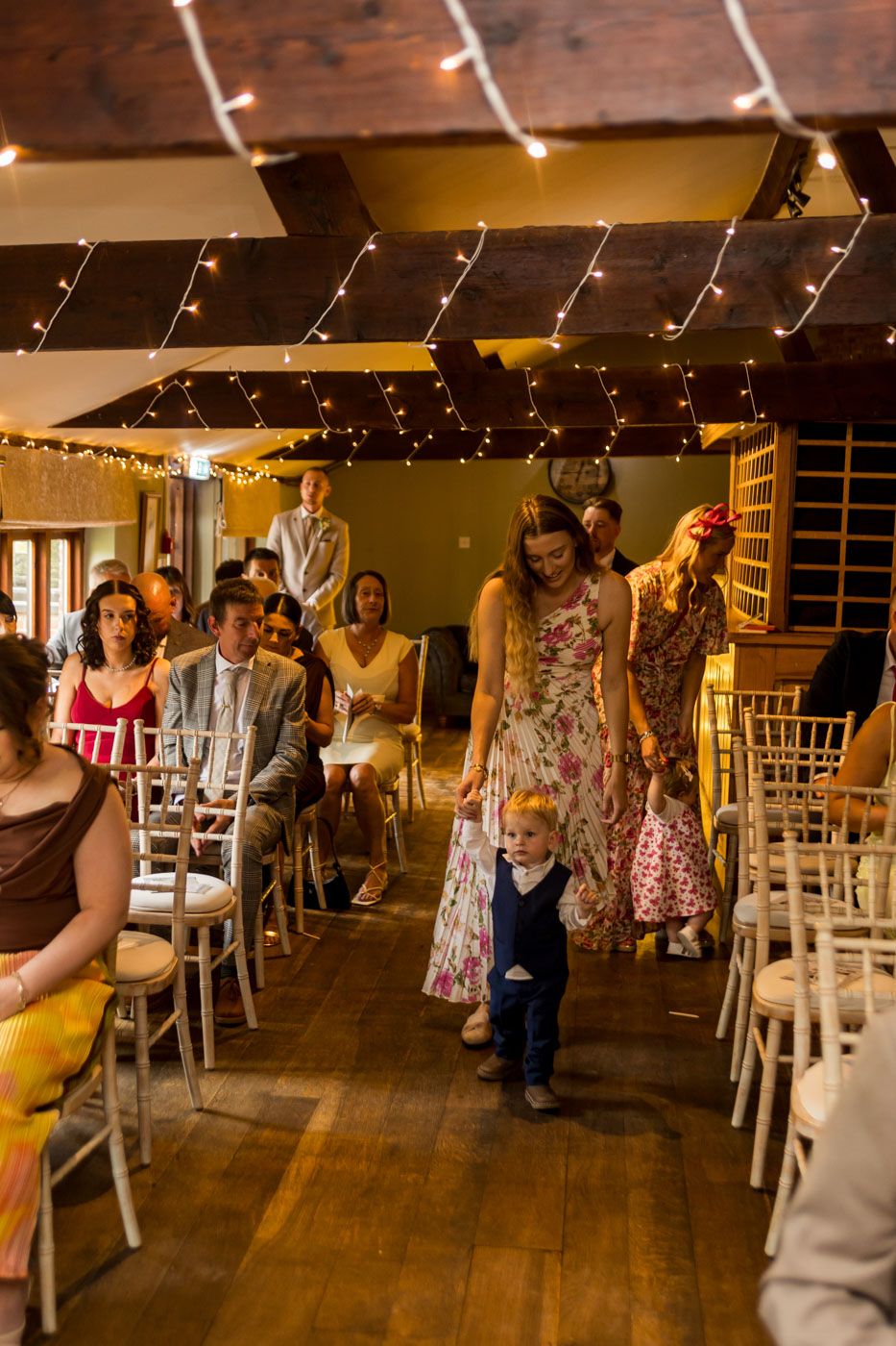 Wedding guests mingling in a rustic venue with wooden floors and string lights.