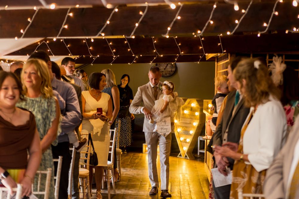 Wedding guests gather in a rustic venue decorated with twinkling string lights for a celebration.