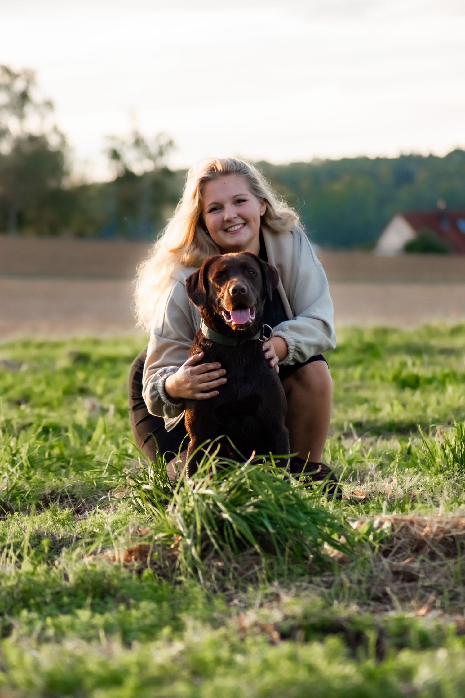 A happy black Labrador and their owner share a joyful moment in a sunlit field during golden hour.