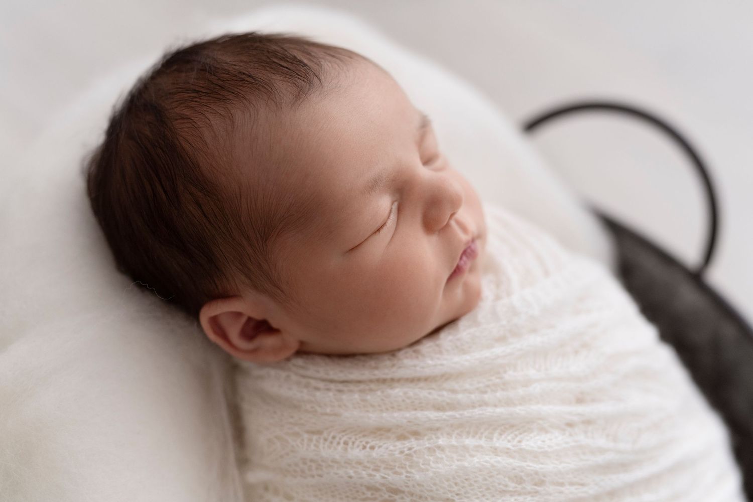 Backlit newborn baby wrapped in white swaddle blanket during professional photography session.