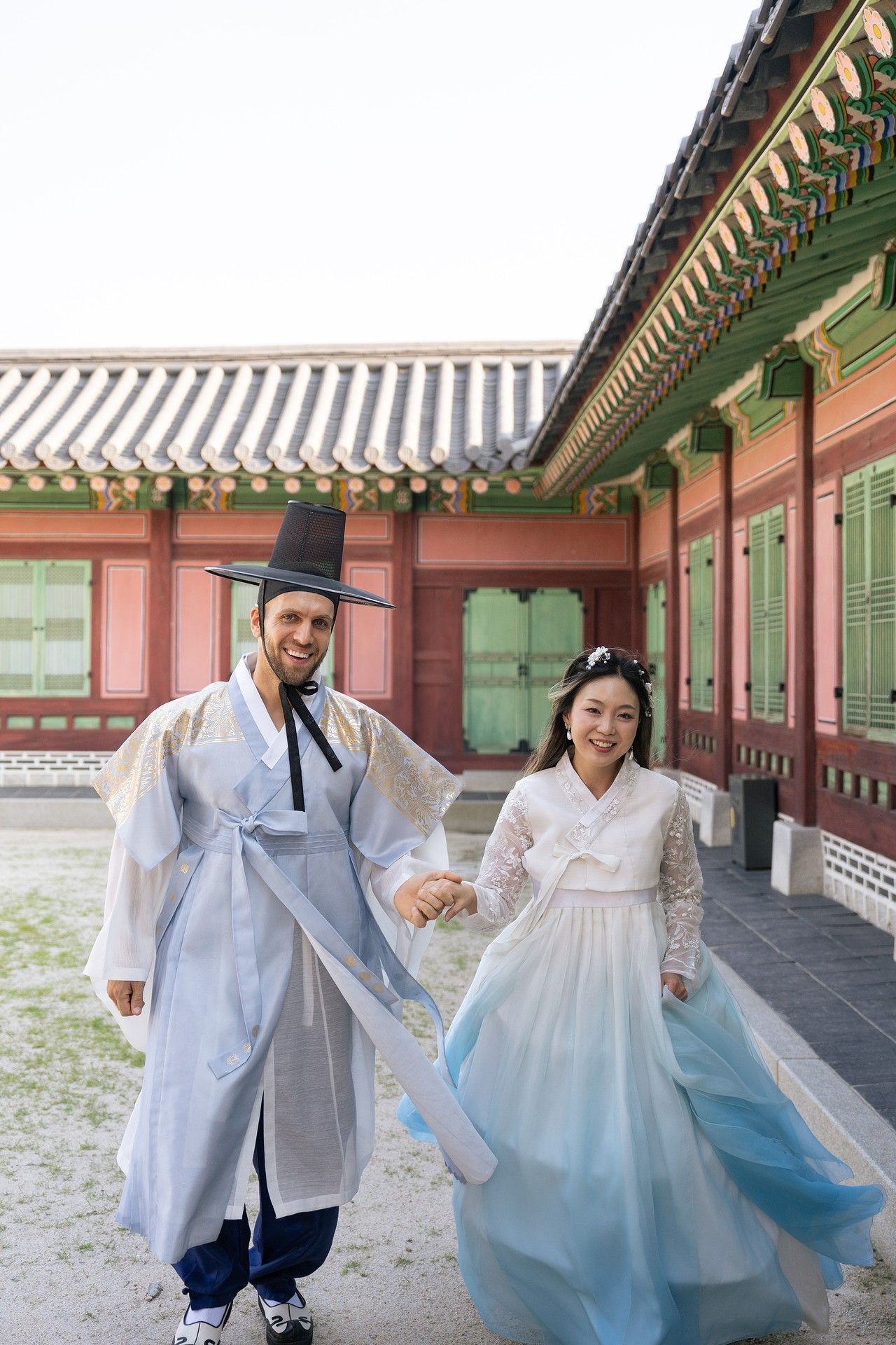 Traditional Korean hanbok-wearing couple walks through ornate palace corridor with wooden beams and painted details.